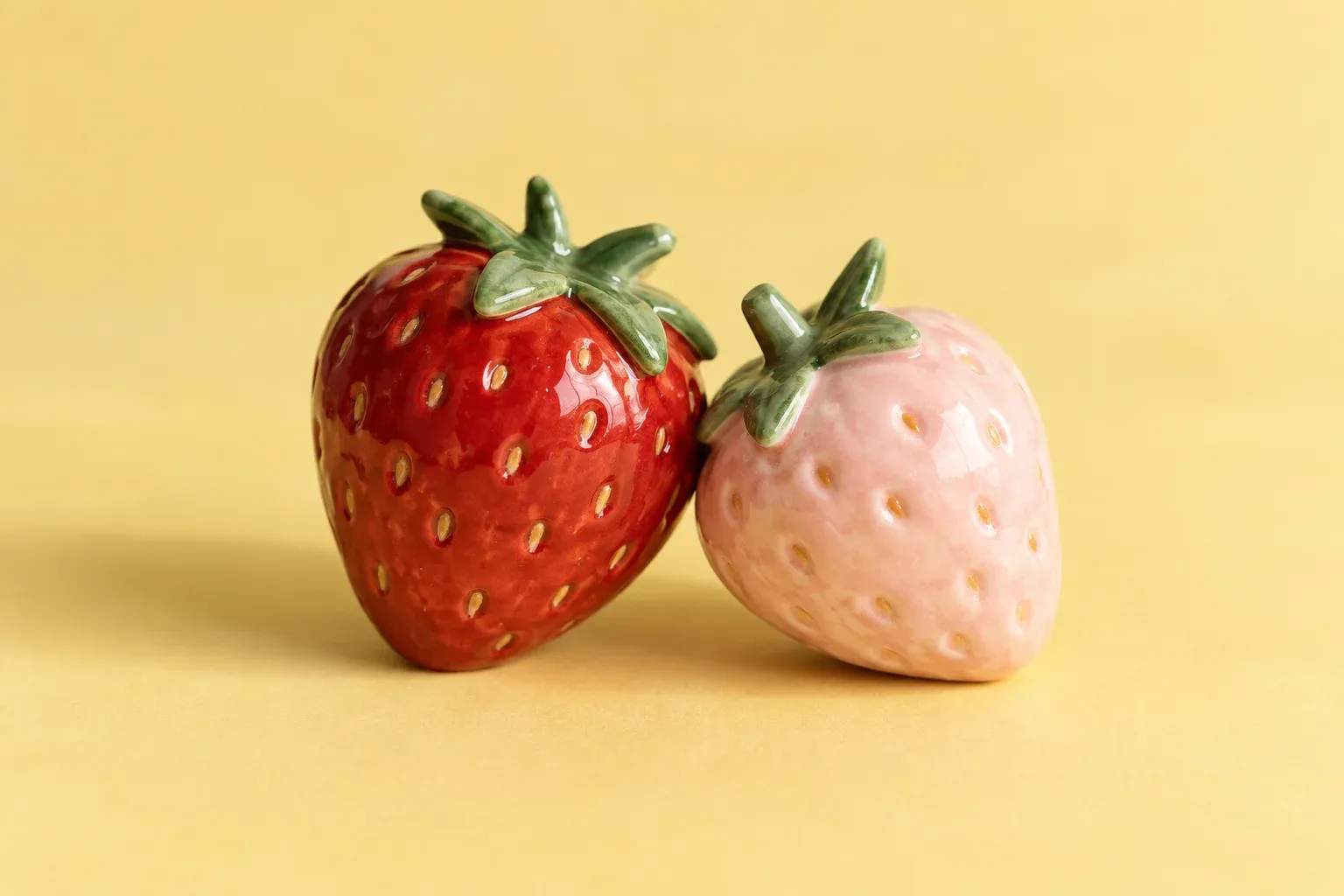 Two handmade ceramic strawberries leaning together on a yellow surface.