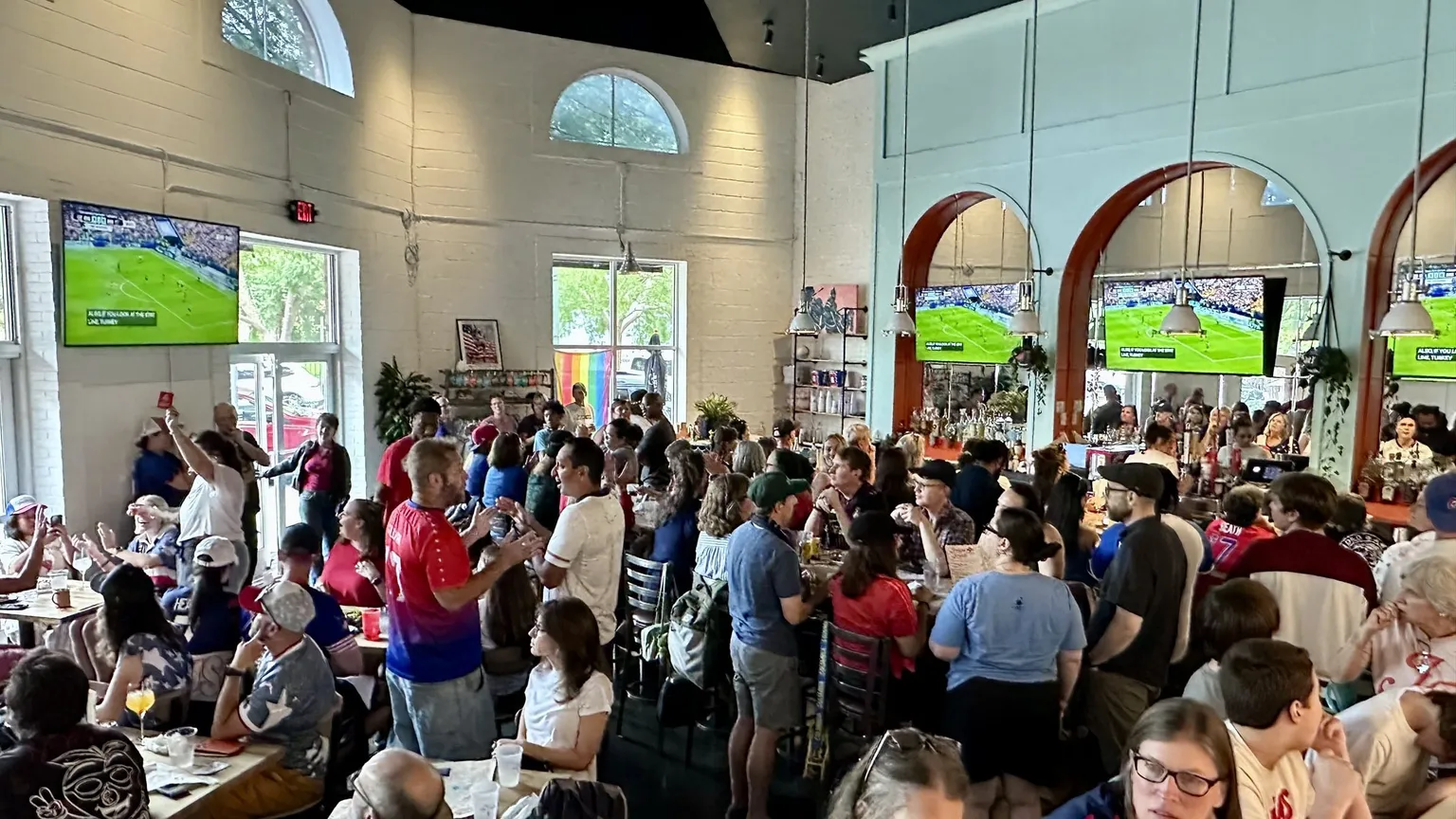 A packed watch party at Jolene Jolene, with fans filling every table beneath arched screens showing women's sports
