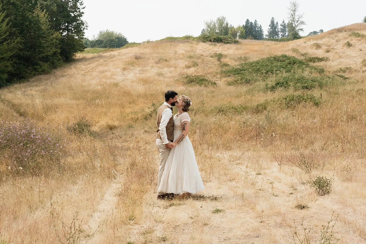 A bride and groom kissing on a hillside of golden summer grass, photographed by KN Captures