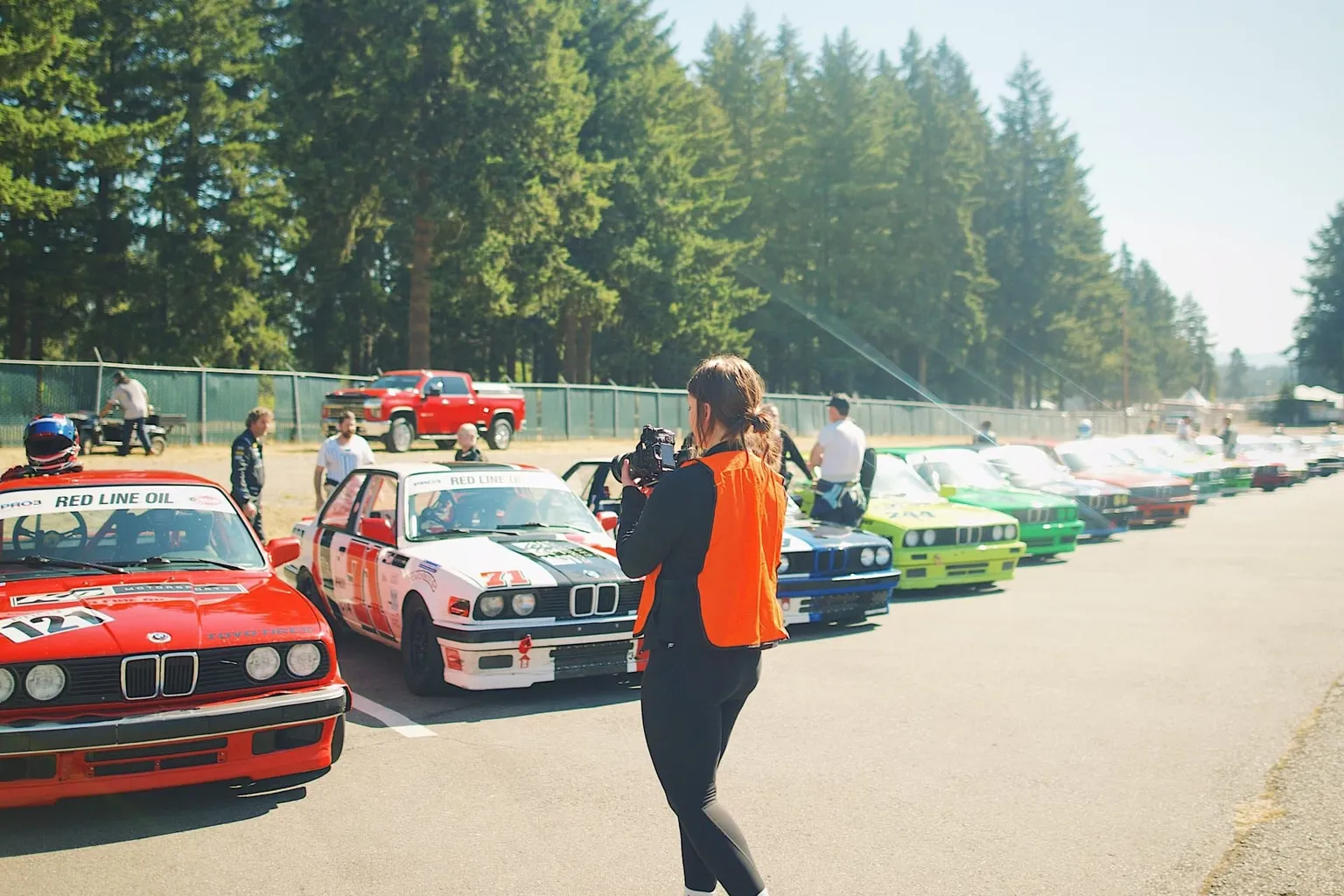 Karmen Trebolo walking a line of vintage BMW race cars with her camera at a track day shoot
