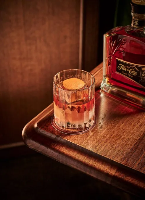 Cocktail with an orange garnish beside a rum bottle, photographed by Guy Davies