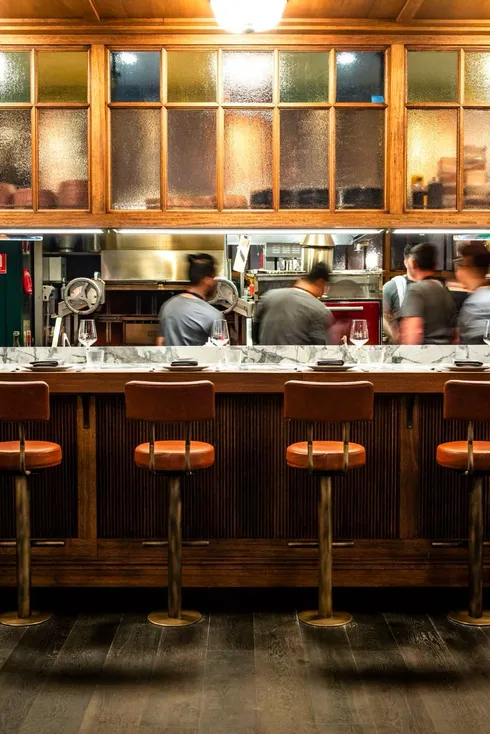 Restaurant bar interior with leather stools and an open kitchen, photographed by Guy Davies