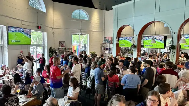 A packed watch party at Jolene Jolene beneath arched screens showing women's sports