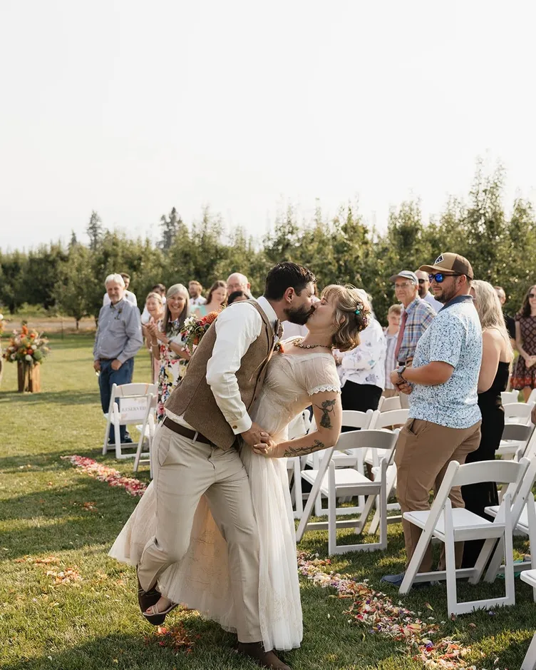 A groom dipping the bride for a kiss in the aisle as guests cheer