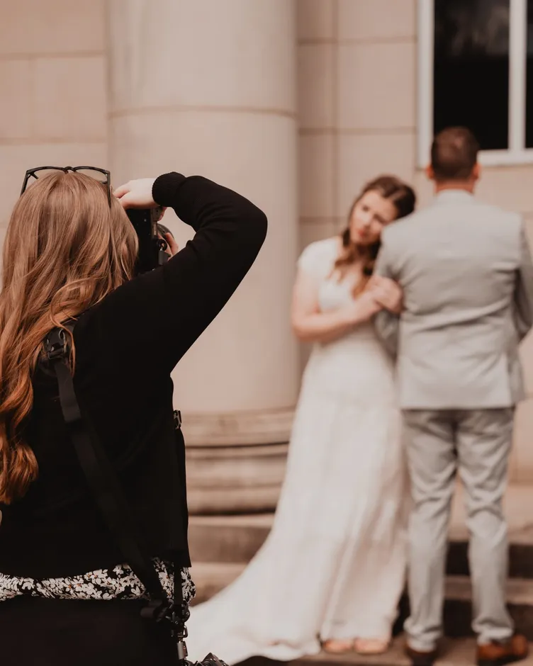 Karmen photographing a bride and groom embracing between stone columns