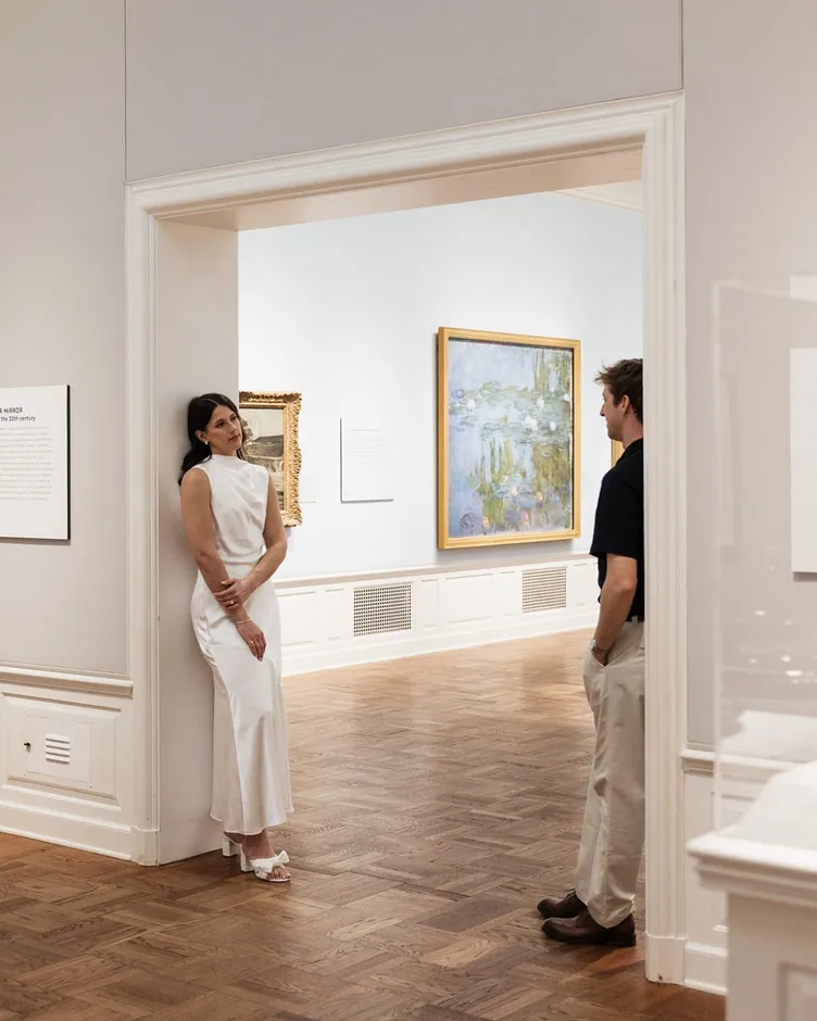 An engaged couple framed by a doorway in an art gallery, a Monet water lilies painting behind them