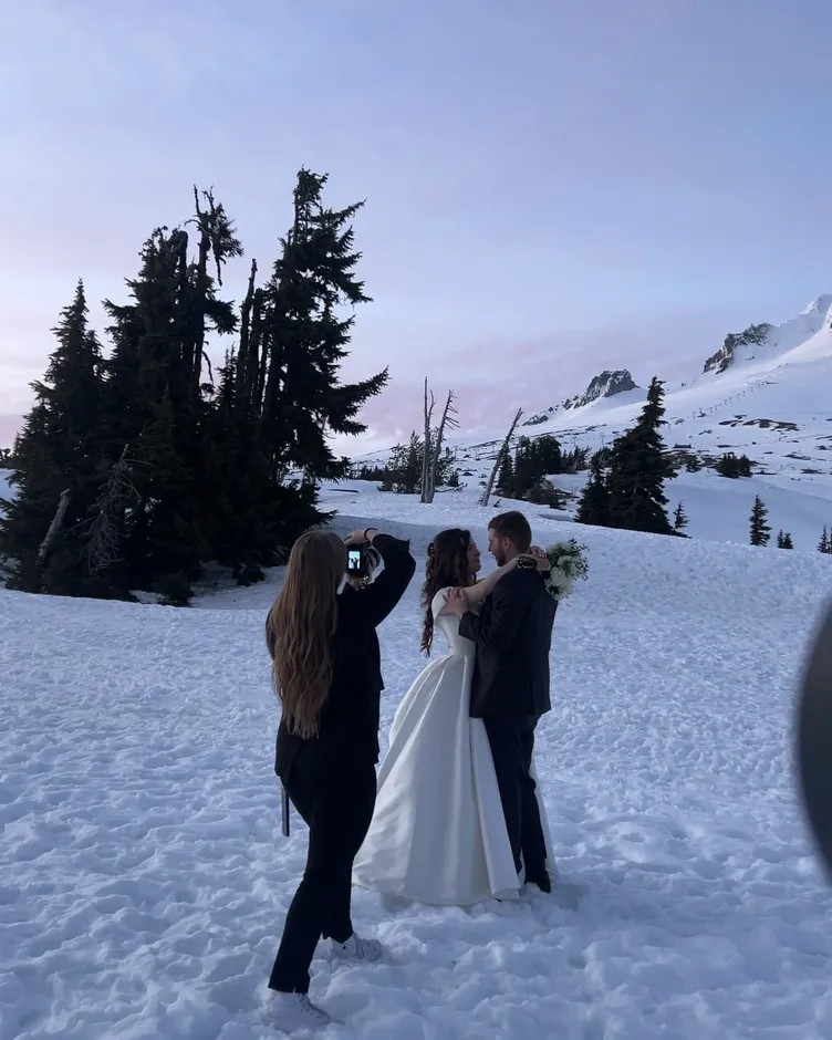 Karmen photographing a couple in wedding attire on a snowy mountainside at dusk