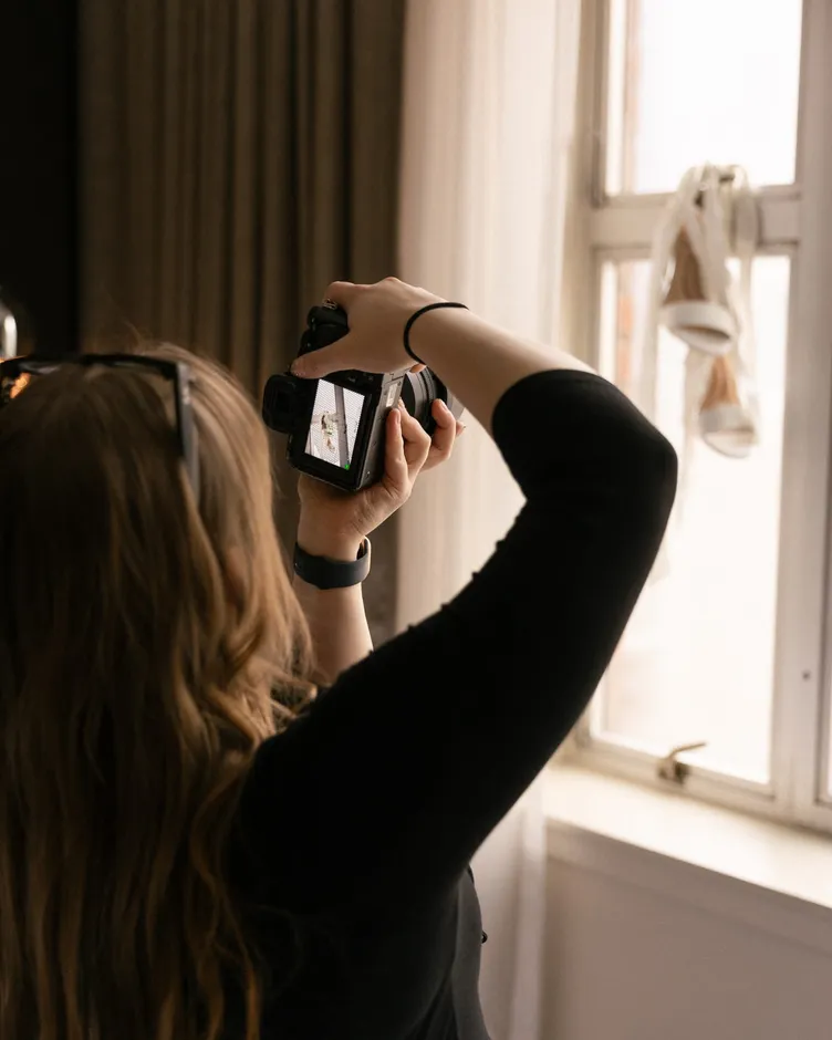 Karmen checking the back of her camera while photographing bridal shoes hung in a window