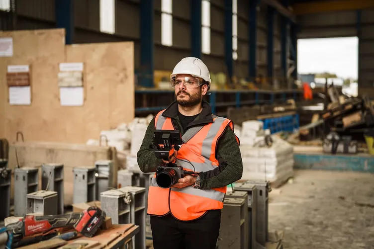 One of the Oh Brother team filming on a construction site in a hard hat and hi-vis vest