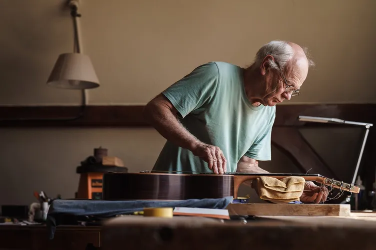 Luthier stringing a handmade guitar in his London workshop