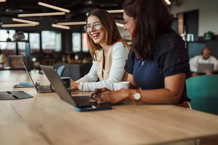 Two colleagues laughing at a laptop during an office photography shoot