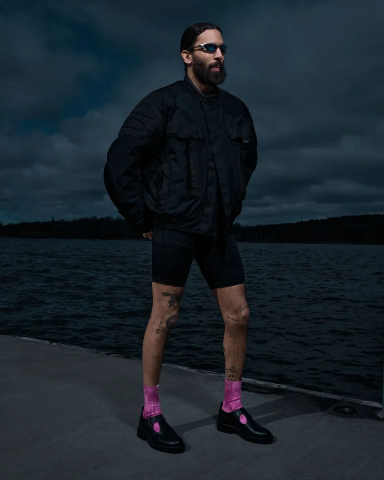 Model in a black jacket wearing pink SOCKSSS socks with black shoes by the water