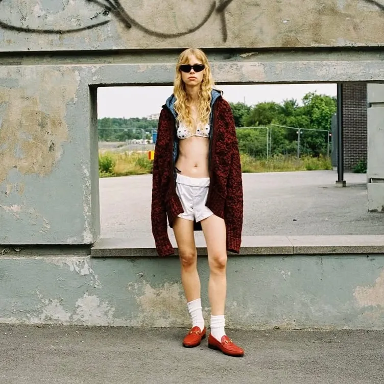 Model wearing white SOCKSSS socks with red loafers in an urban setting