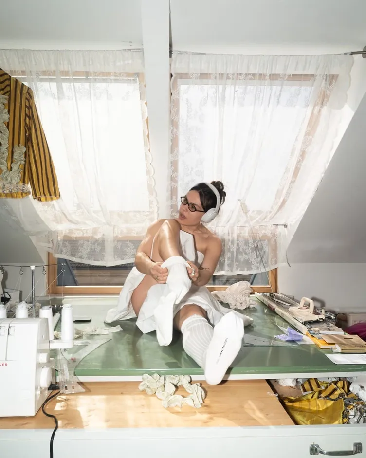 Designer sitting on a cutting table in her studio pulling on white SOCKSSS socks