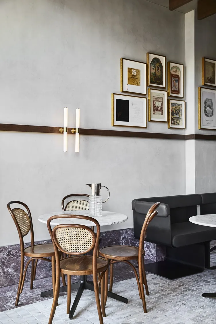 A cafe corner by Studio Terrando, with bentwood chairs, marble tables and a gallery wall on textured plaster