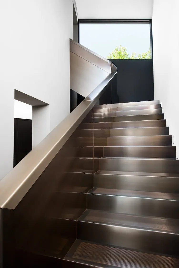 A bronze staircase in a Studio Terrando residence, lit from a window above