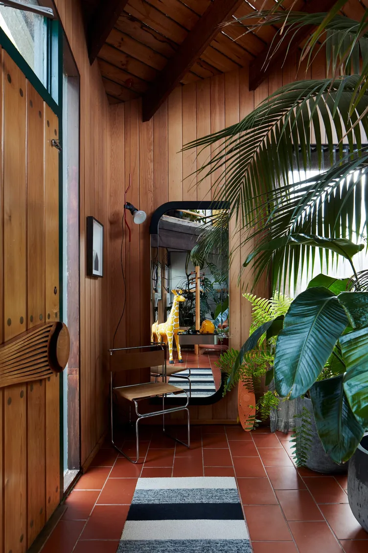 A plant-filled timber hallway by Studio Terrando with a rounded mirror and terracotta floor tiles