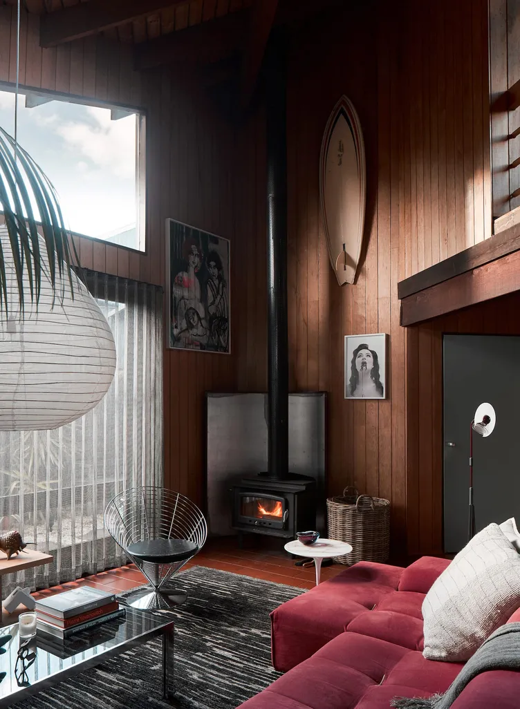 A timber-clad living room by Studio Terrando with a wood fire, surfboard on the wall and red sofa
