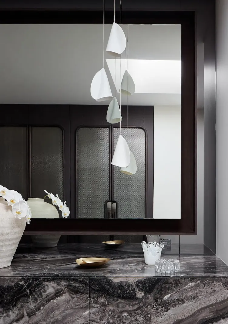 A marble vanity with sculptural pendant lights and a dark timber mirror by Studio Terrando