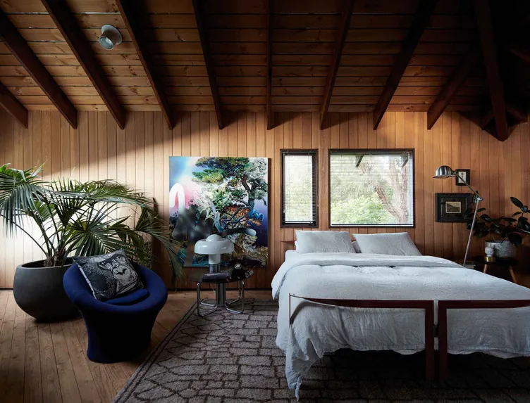 A timber-panelled bedroom by Studio Terrando with a large artwork, vintage lamp and layered textiles