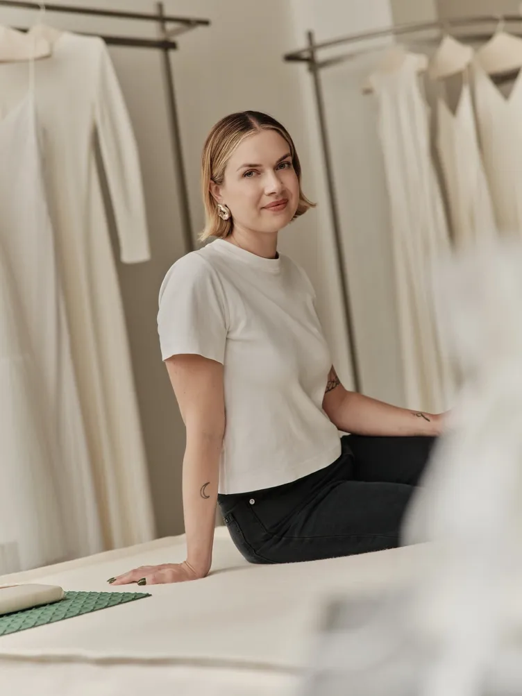 Annelise Sealy, founder of The Fall Bride, seated between racks of ivory gowns in the Brooklyn store