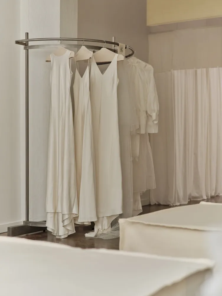 Silk gowns and a sheer organza piece on a curved steel rack at The Fall Bride