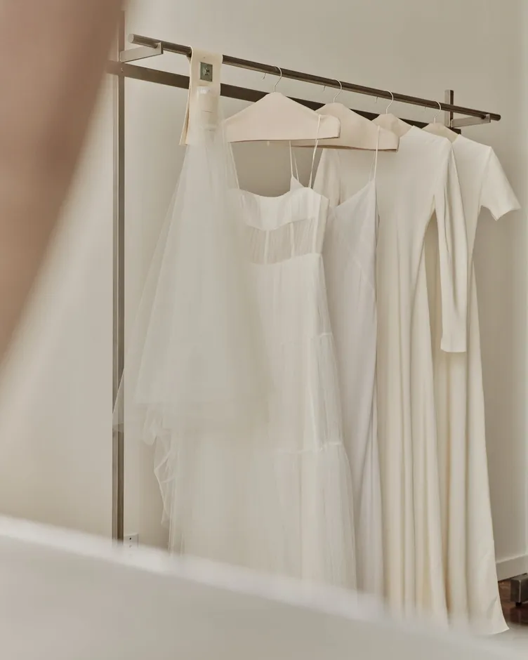 A veil and modern gowns on canvas hangers along a steel rack at The Fall Bride