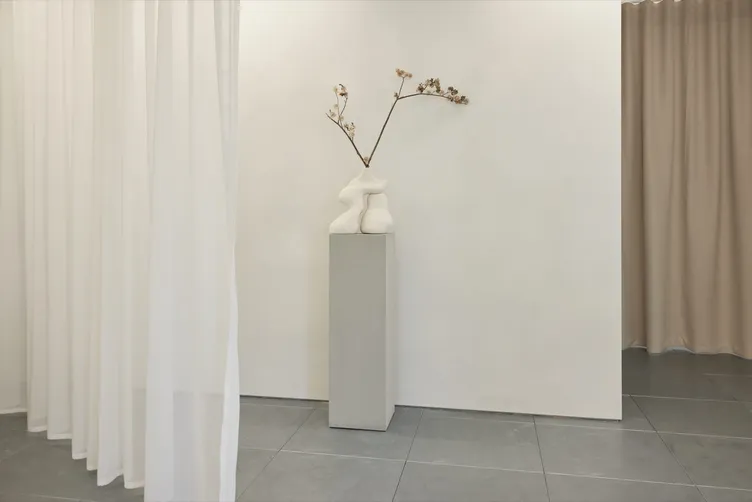 A sculptural vase with dried blossom on a plinth between sheer curtains at The Fall Bride